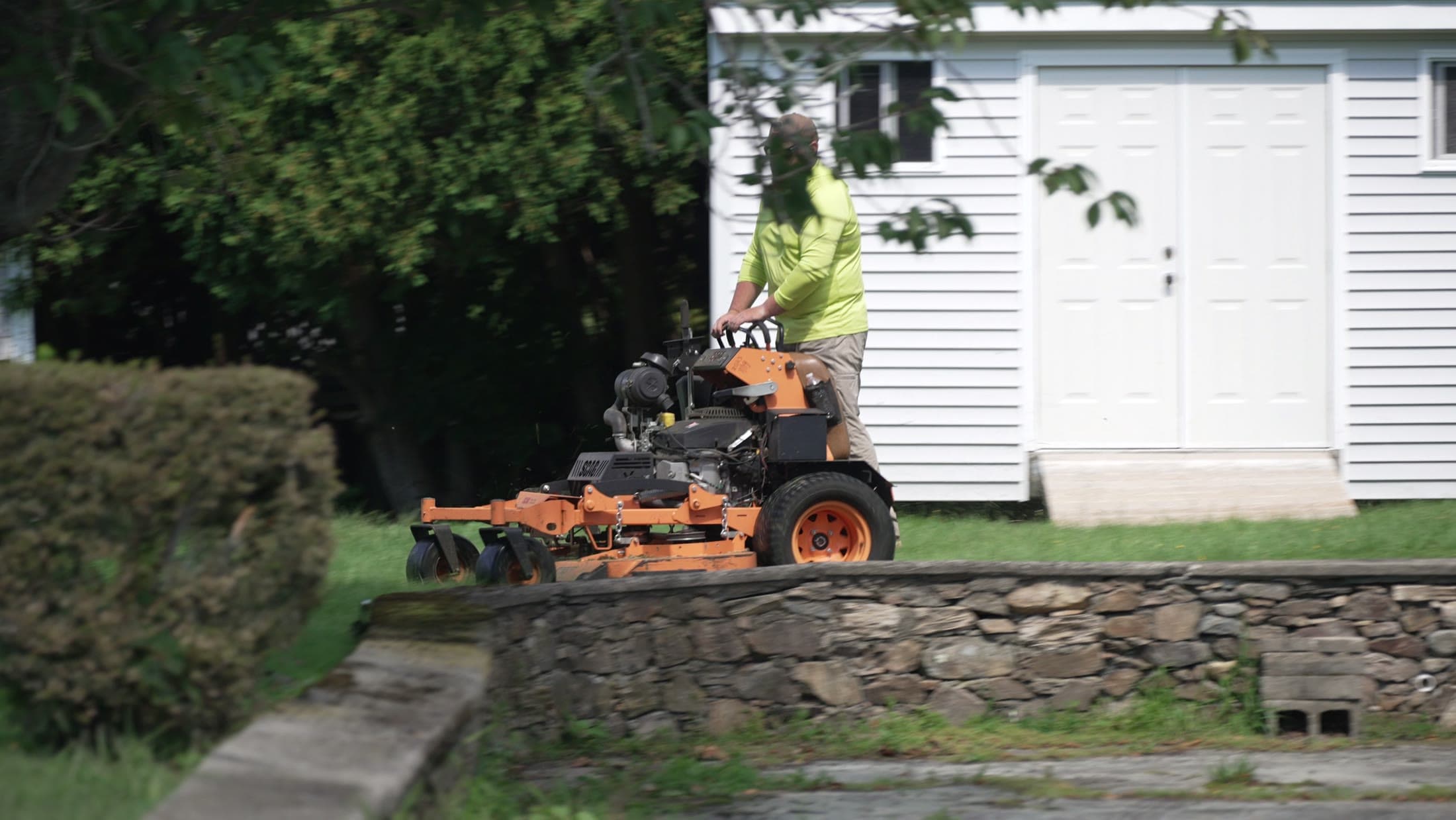 A mower cutting the lawn along the top of a stone wall