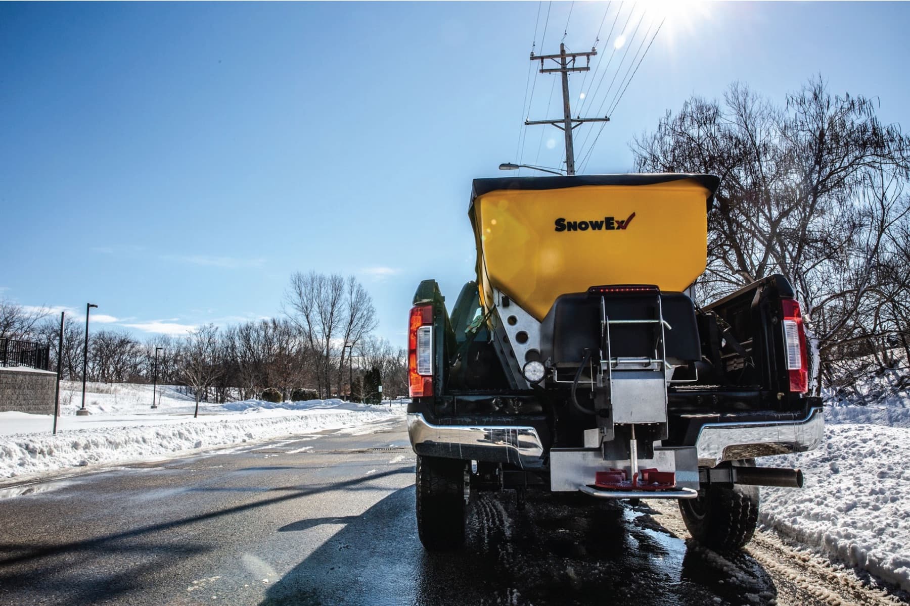 A truck-bed salt spreader ready to treat cleared surfaces on a sunny winter day