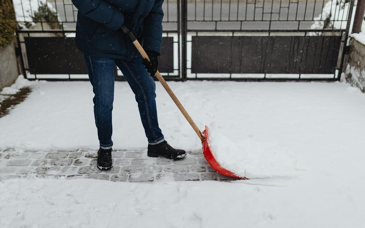 A worker clearing snow from a paved walkway with a shovel