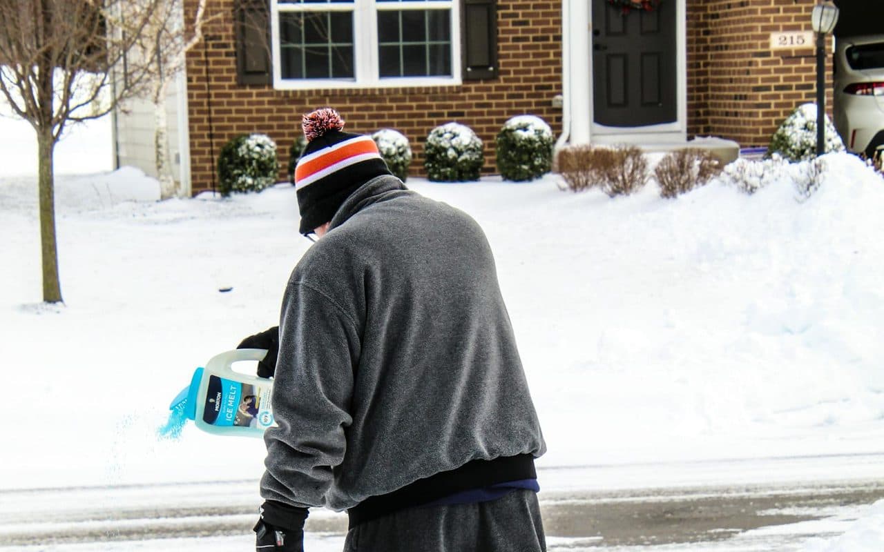 Ice melt being spread by hand across a cleared residential driveway