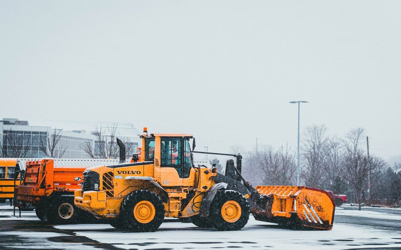 A wheel loader with a plow attachment clearing snow from a commercial parking lot
