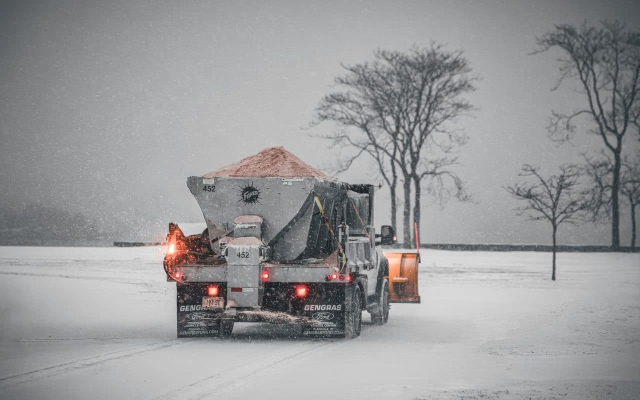 A spreader truck loaded with salt treating a lot during a snowstorm