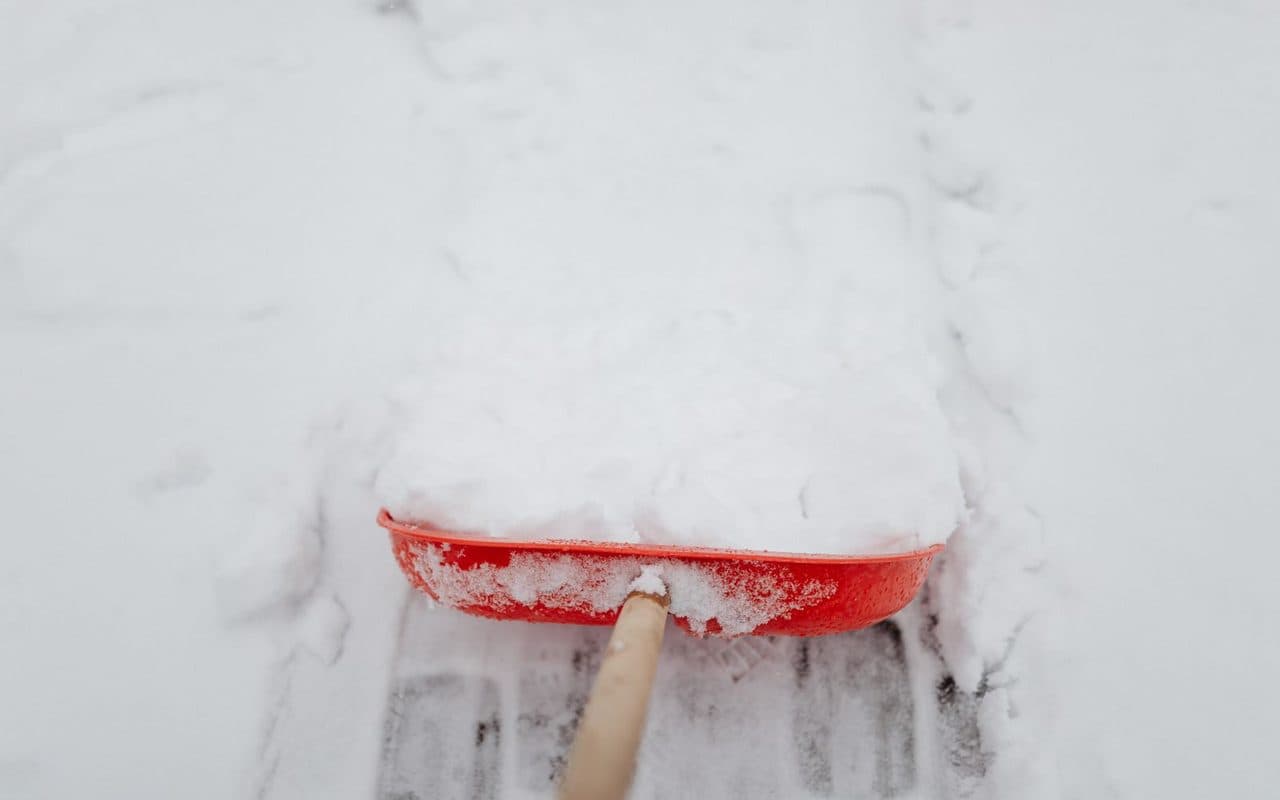 A snow shovel pushing a clean load of fresh snow off a paved surface