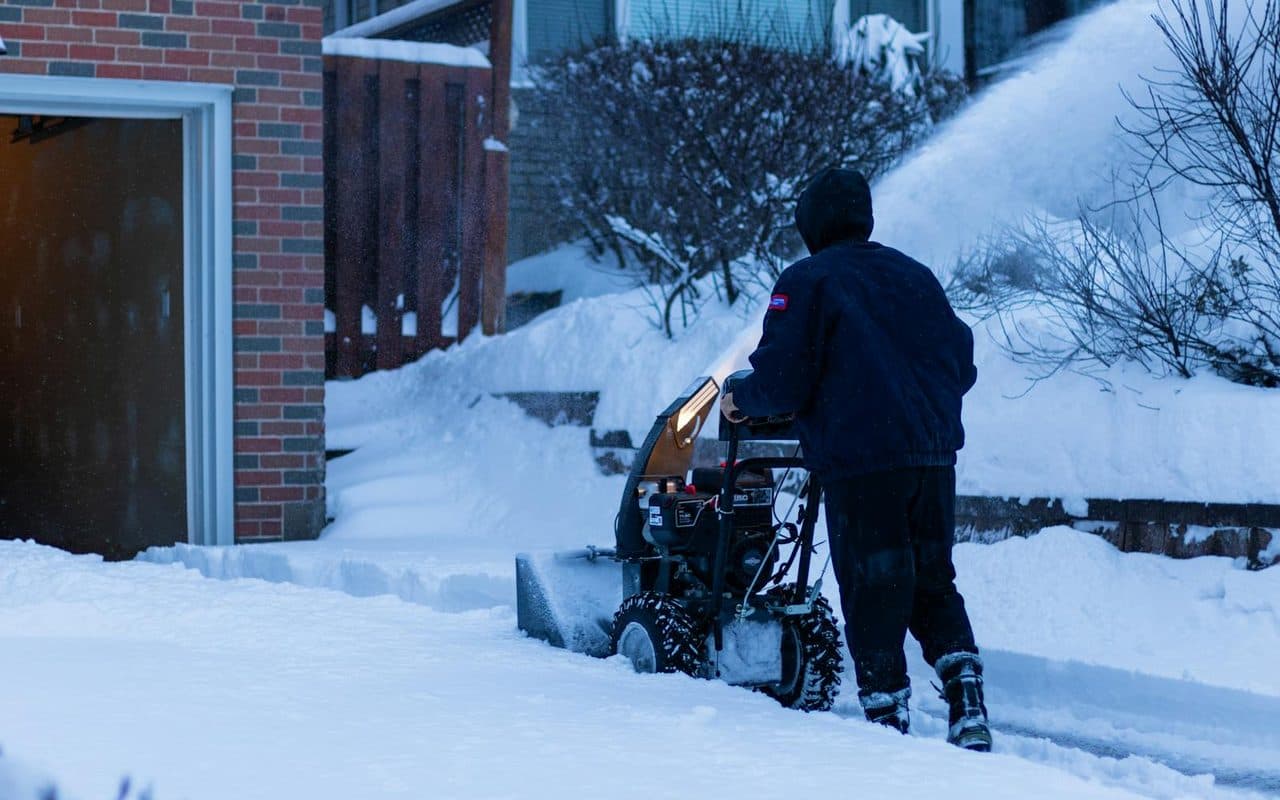 A snowblower clearing deep snow from a walkway beside a home