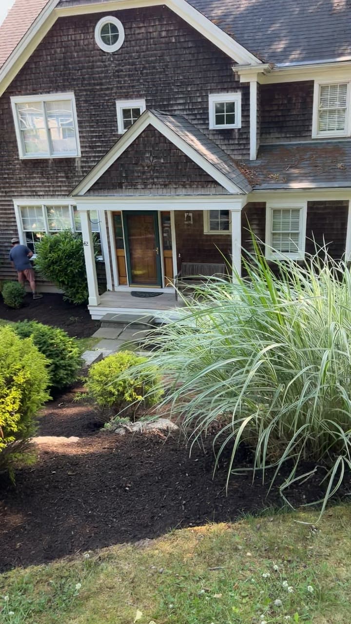 A long, freshly mulched and cleaned planting bed beside a manicured waterfront lawn