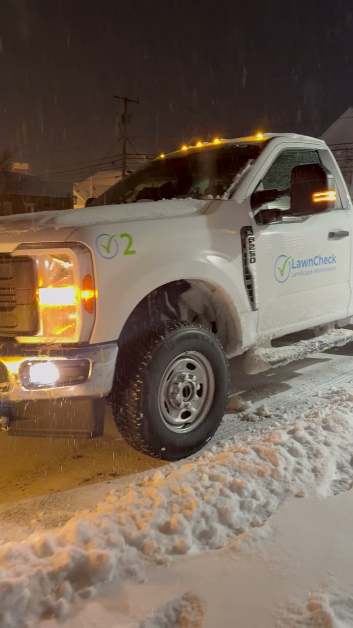 A LawnCheck plow truck clearing a snow-covered driveway at night in the East Bay, Rhode Island