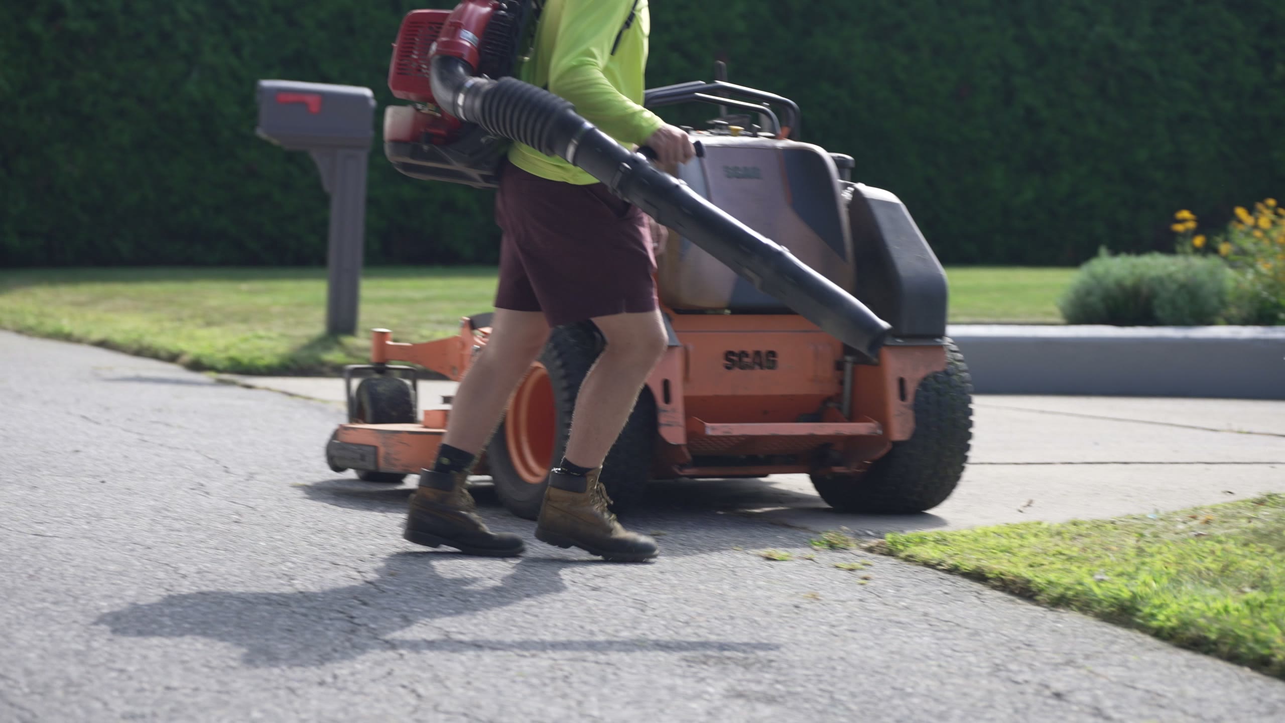 A crew member with a backpack blower walking past the mower on a driveway