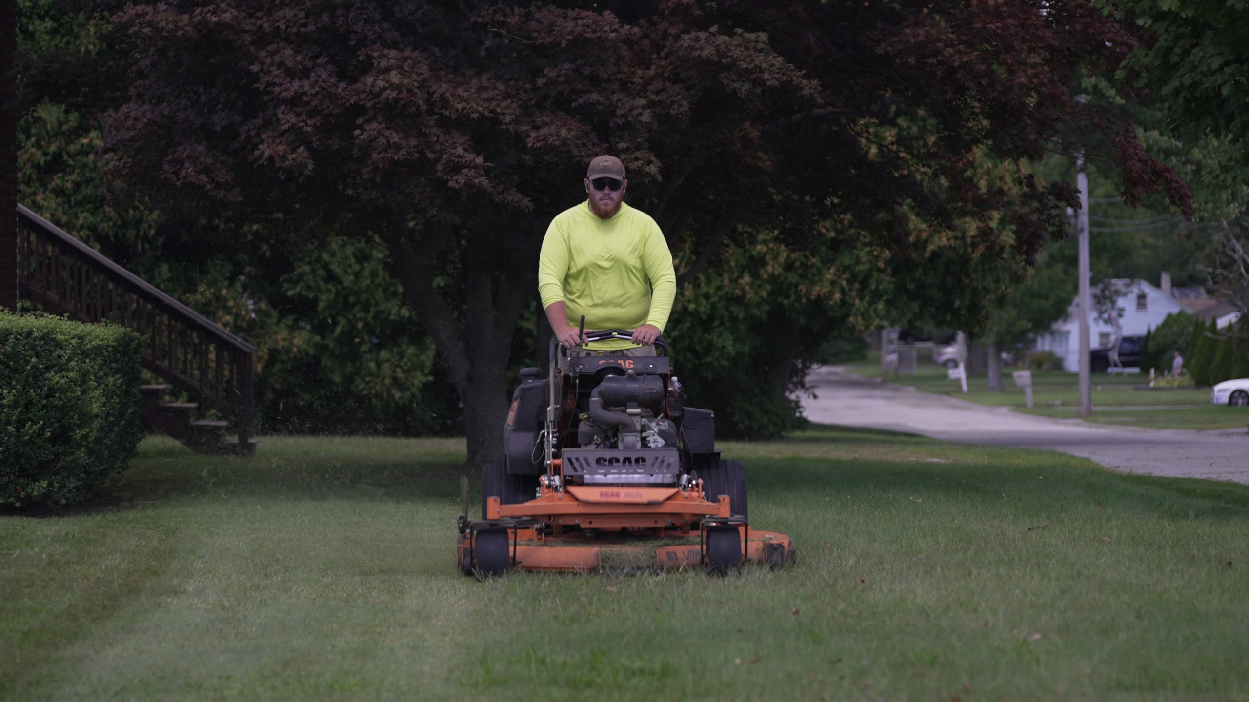 A crew member on the mower, mid pass across a front lawn