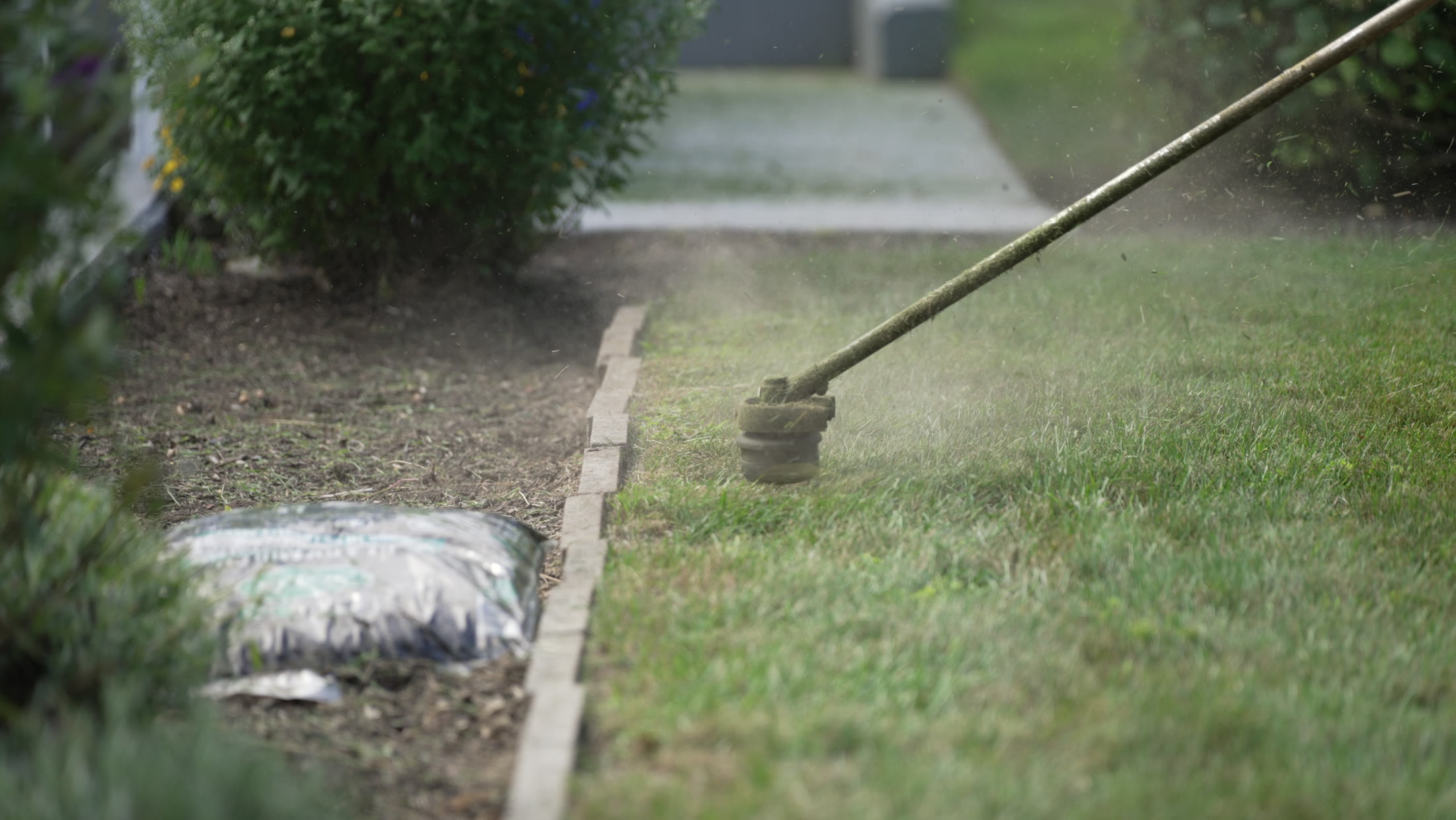 A string trimmer cutting a clean lawn edge along a bed border